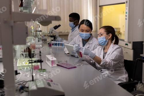Preview: Two intercultural women in masks and labcoats working in team