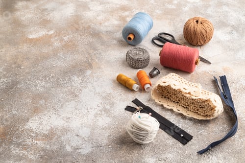 Preview: Sewing accessories: scissors, thread, thimbles, braid on brown concrete background. Side view