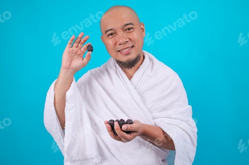 Preview: Smiling Muslim Pilgrim in White Ihram Showing One Date Fruit While Holding More in Hand