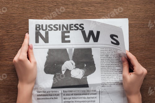 Preview: cropped image of journalist reading business newspaper at wooden table