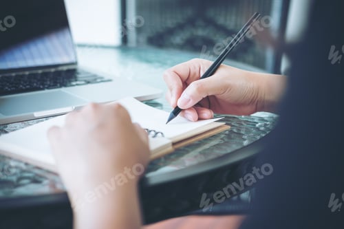 Preview: A woman working and holding black pencil and writing on notebook on glass table