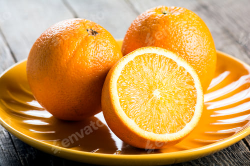 Preview: Closeup of ripe orange fruits sliced on a yello plate on a wooden table