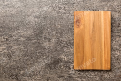 Preview: Top view of wooden cutting board on cement background. Empty space for your design