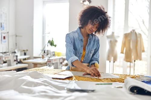 Preview: African-American seamstress works with sewing patterns and yellow fabric at cutting table