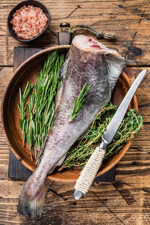 Preview: Raw cod or codfish fish in wooden plate with herbs. Wooden background. Top view