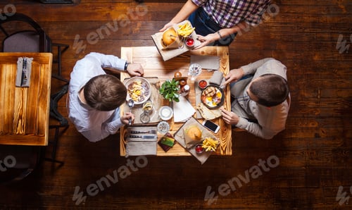 Preview: Young men having meal at cafe, waitress bringing their order