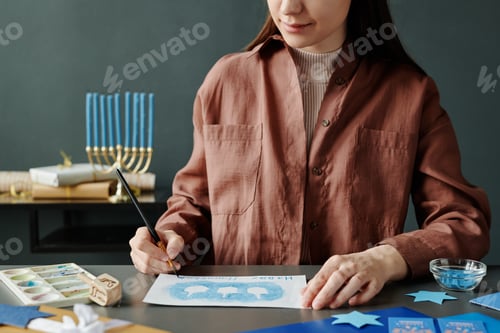 Preview: Cropped shot of young woman in brown shirt writing down Hanukkah wish