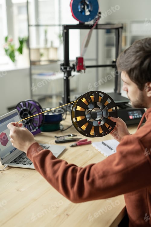 Preview: Designer stretching yellow filament from spool while choosing color for printing