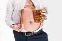 Vorschau: Teilansicht eines übergewichtigen Mannes, der Bauch zeigt und ein Glas Bier mit gegrillter Wurst hält