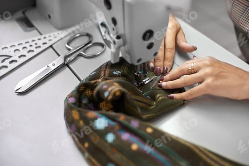 Preview: Seamstress working on modern electrical sewing machine making exclusive garments in fashion studio.