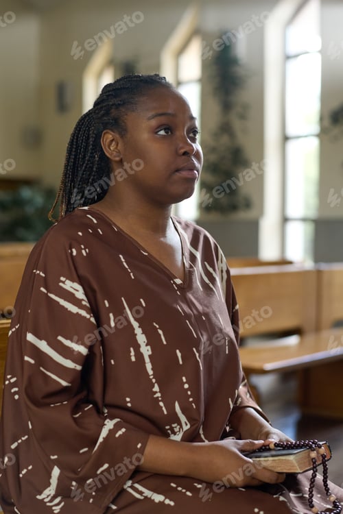 Preview: Young serious woman in brown dress holding Holy Bible and rosary beads