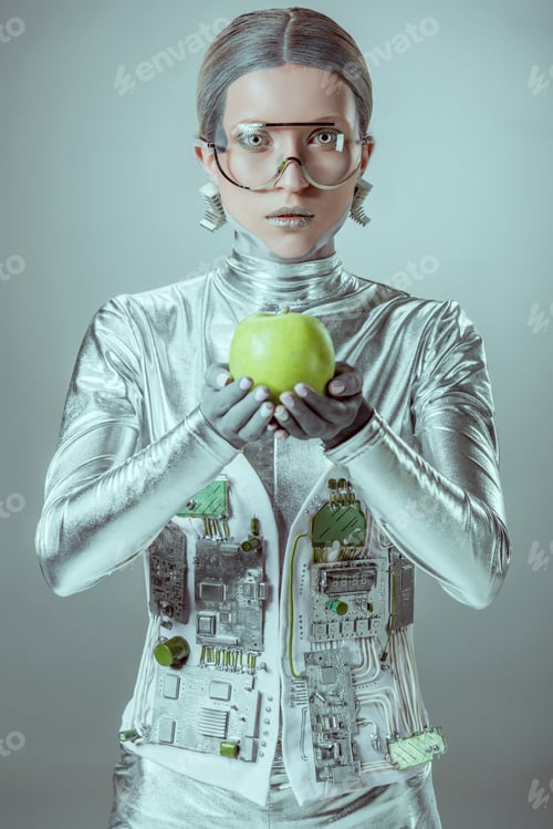 Preview: cyborg in futuristic eyeglasses holding apple and looking at camera isolated on grey, future