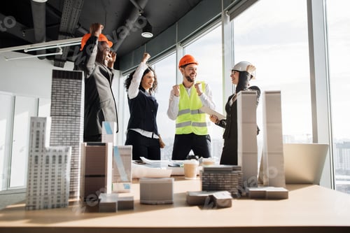 Preview: Successful team of coworkers builders and architects are raising hands in fists and screaming