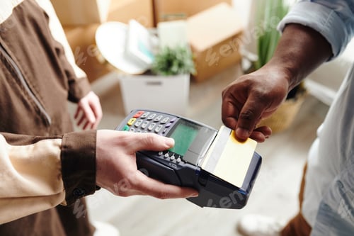 Preview: Hand of young man in workwear holding payment terminal while African male paying for loading service