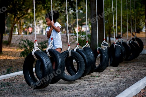 Preview: A curly girl black skin playing on passes an obstacle on tires in a rope Park.