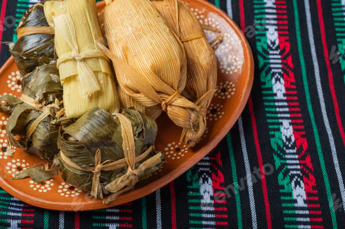 Preview: Different tamales in a clay dish on a tablecloth with the colors of the Mexican flag.