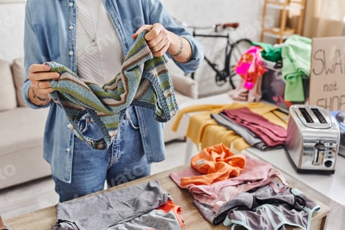 Preview: exchange market, partial view of tattooed woman sorting clothing and holding knitted tank top
