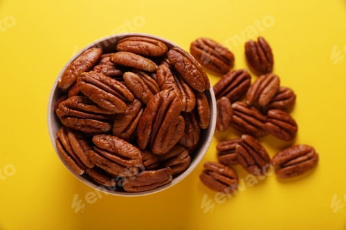 Preview: Tasty pecan nuts with bowl on yellow background, flat lay