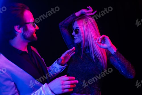 Preview: Stylish coupe in sunglasses dancing isolated on black with colorful lighting
