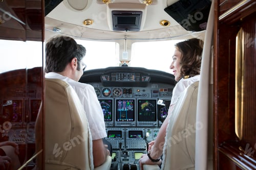 Preview: Rear view of male and female pilots talking in cockpit of private jet