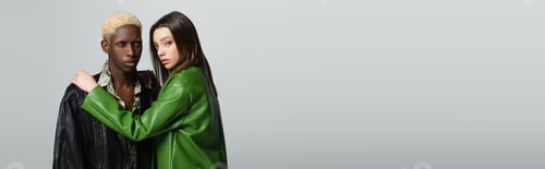 Preview: brunette woman in green leather jacket hugging blonde african american man isolated on grey, banner