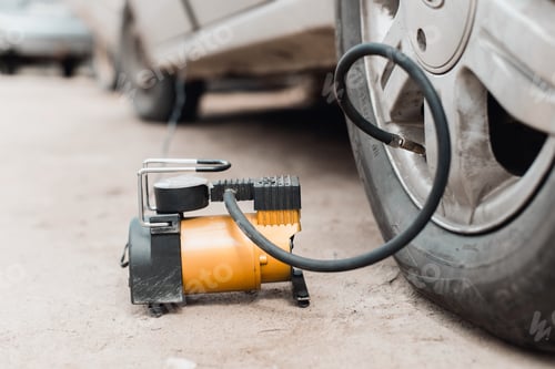 Preview: Wheel repair, pumping air into tire with car compressor outdoors. Close-up, low angle view