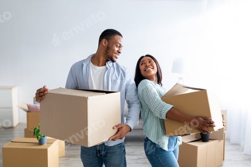 Preview: Home relocation concept. Loving african american couple carrying carton boxes in their new house