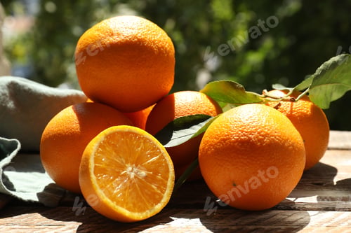 Preview: Fresh whole and cut oranges on wooden table against blurred green background, closeup