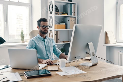 Preview: Inspired to work hard. Young modern businessman working using computer while sitting in the office