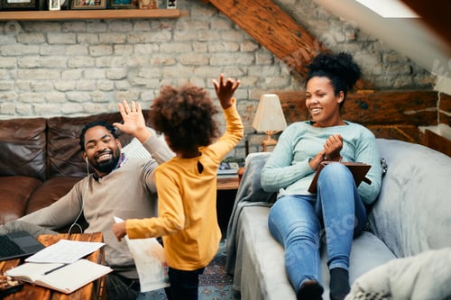 Preview: Happy African American father giving high-five to his daughter while working on laptop at home.