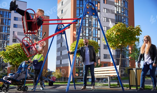Preview: Happy family - father, mother and children having fun together on playground.