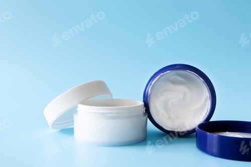 Preview: Opened moisturizer cream in white plastic jars on blue background