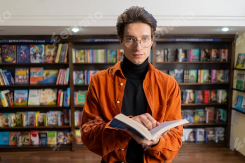 Preview: portrait of a young guy in glasses with a book in his hands in the library preparing exams