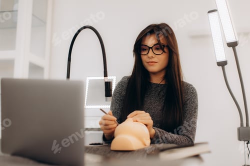 Preview: Woman learning cosmetology online with mannequin and laptop
