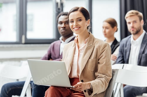 Preview: selective focus of attractive woman in formal wear holding laptop during conference