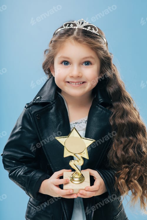 Preview: Positive smiling European child with blue eyes, long crisp hair, holds reward in form of star.
