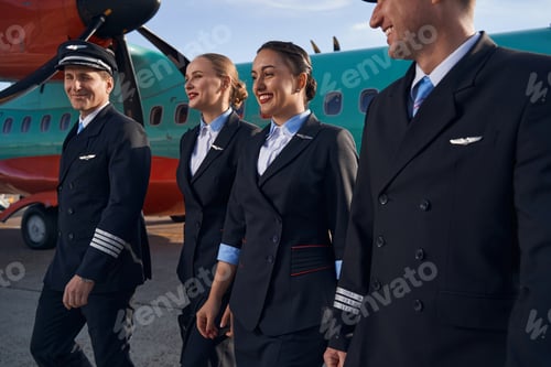 Preview: Smiling airplane crew members walking together on runway