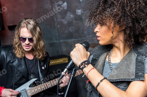 Preview: side view of woman singing in microphone with man playing guitar, rock and roll girl concept
