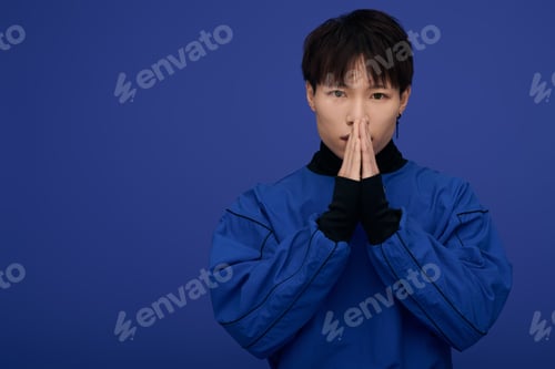 Preview: Young Asian man expresses gratitude against a vibrant blue backdrop during a creative session