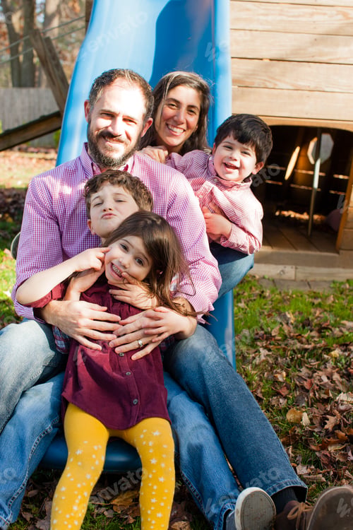 Preview: Family in a row between each others legs on playground slide, looking at camera smiling