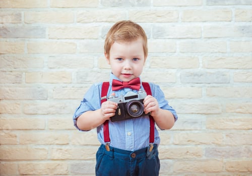 Preview: Cute little boy standing with retro camera on brick wall background