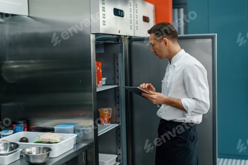 Preview: Professional chef using tablet computer for recipes while working in modern kitchen cooking concept
