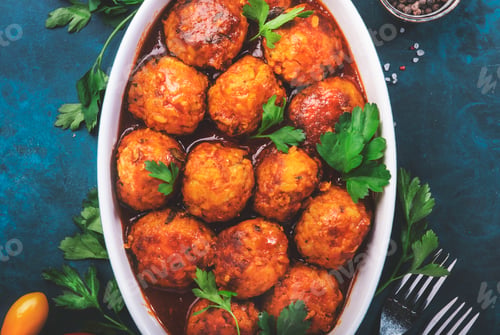 Preview: Meatballs with spicy tomato sauce in white baking dish on blue kitchen table. Top View