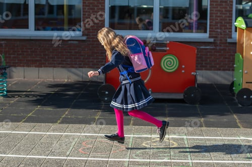 Preview: Schoolgirl with backpack plays hopscotch in the schoolyard,cheerfully jumping on chalk-drawn squares