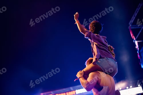 Preview: Back view of couple attending open air music concert at night.