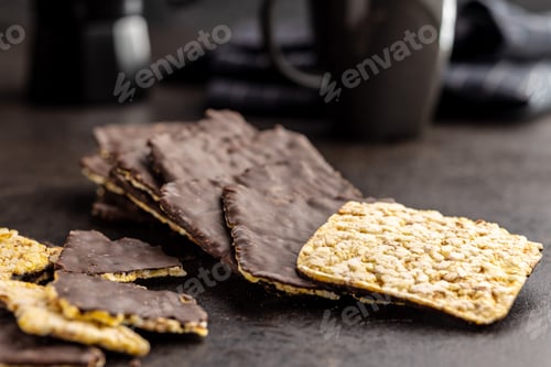 Preview: Puffed corn crackers chocolate covered on black table.