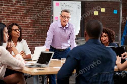 Preview: Mature Businessman Leading Office Meeting Of Colleagues Sitting Around Table