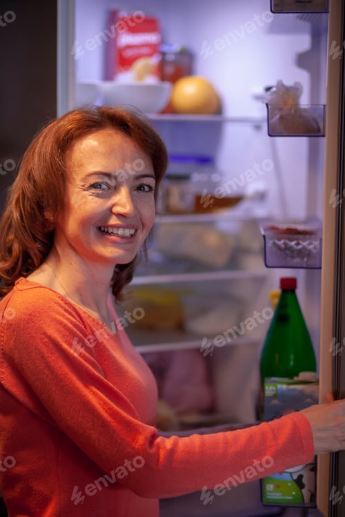 Preview: One Smiling Woman, Looking At Camera, While Holding Refrigerator Door Open. Food And Other Items