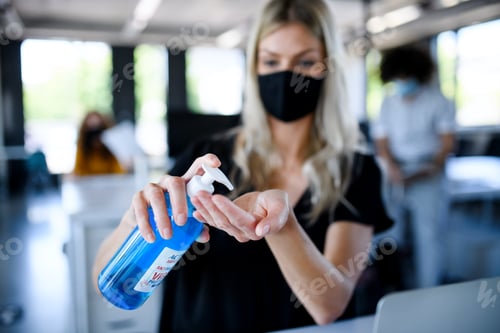 Preview: Young woman with face mask back at work in office after lockdown, disinfecting hands
