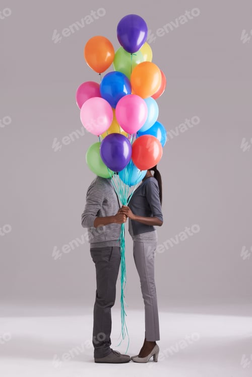 Preview: Bonding behind balloons. Studio shot of a couple hiding behind a bunch of balloons.